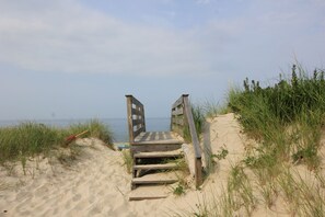 Un escalier en bois mène à une plage de sable bordée de chaque côté par de l’herbe.
