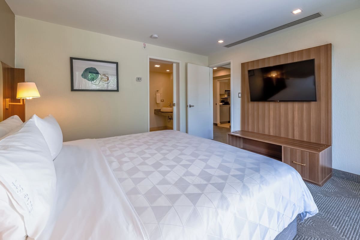 Ein Hotelzimmer mit einem großen Bett, einem an der Wand montierten Fernseher und einem durch eine offene Tür einsehbaren Badezimmer.