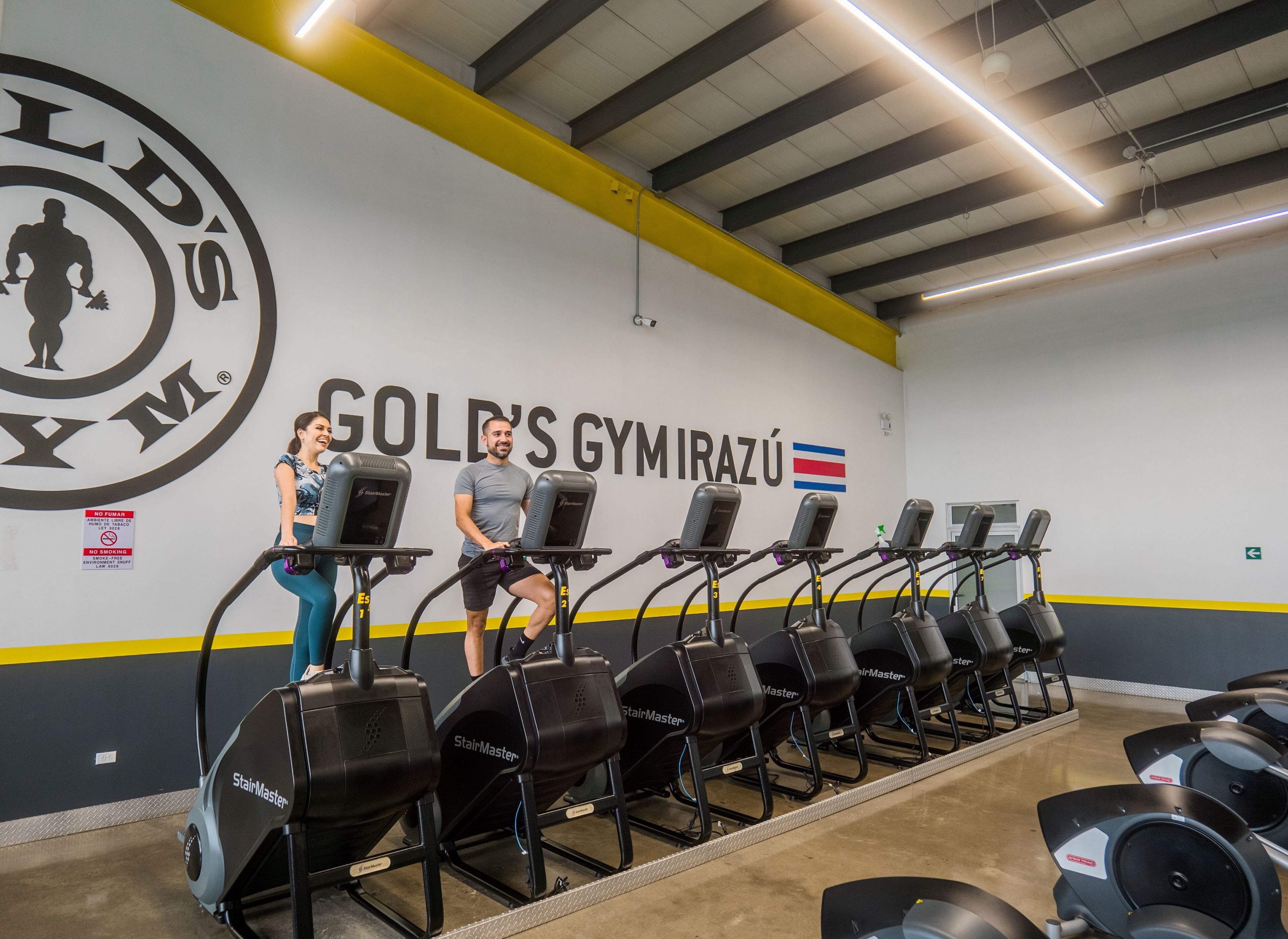 Un gimnasio con cintas de correr y una pared que muestra el nombre "GOLD'S GYMIRAZU".