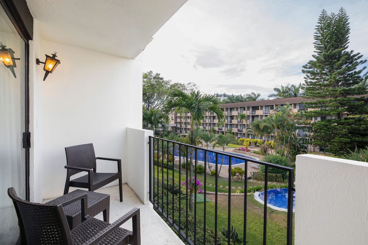 Ein Balkon mit Korbstühlen, ein Pool und Blick auf ein mehrstöckiges Gebäude mit Garten.