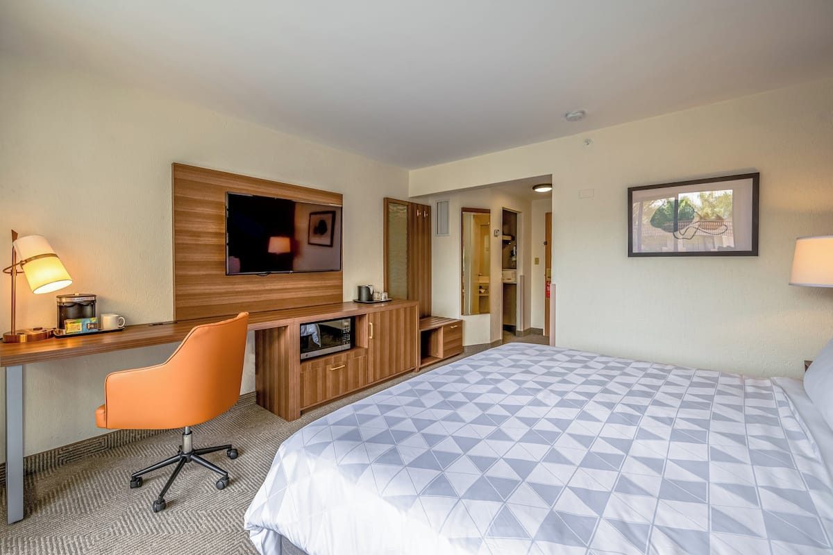 Ein Hotelzimmer mit einem Bett, einem Schreibtisch mit Stuhl, einem Fernseher, einer Mikrowelle und einer Tür zu einem weiteren Raum.