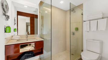 Une salle de bain moderne avec une douche à parois de verre, des toilettes blanches et un meuble-lavabo doté d’un miroir et d’articles de toilette verts.