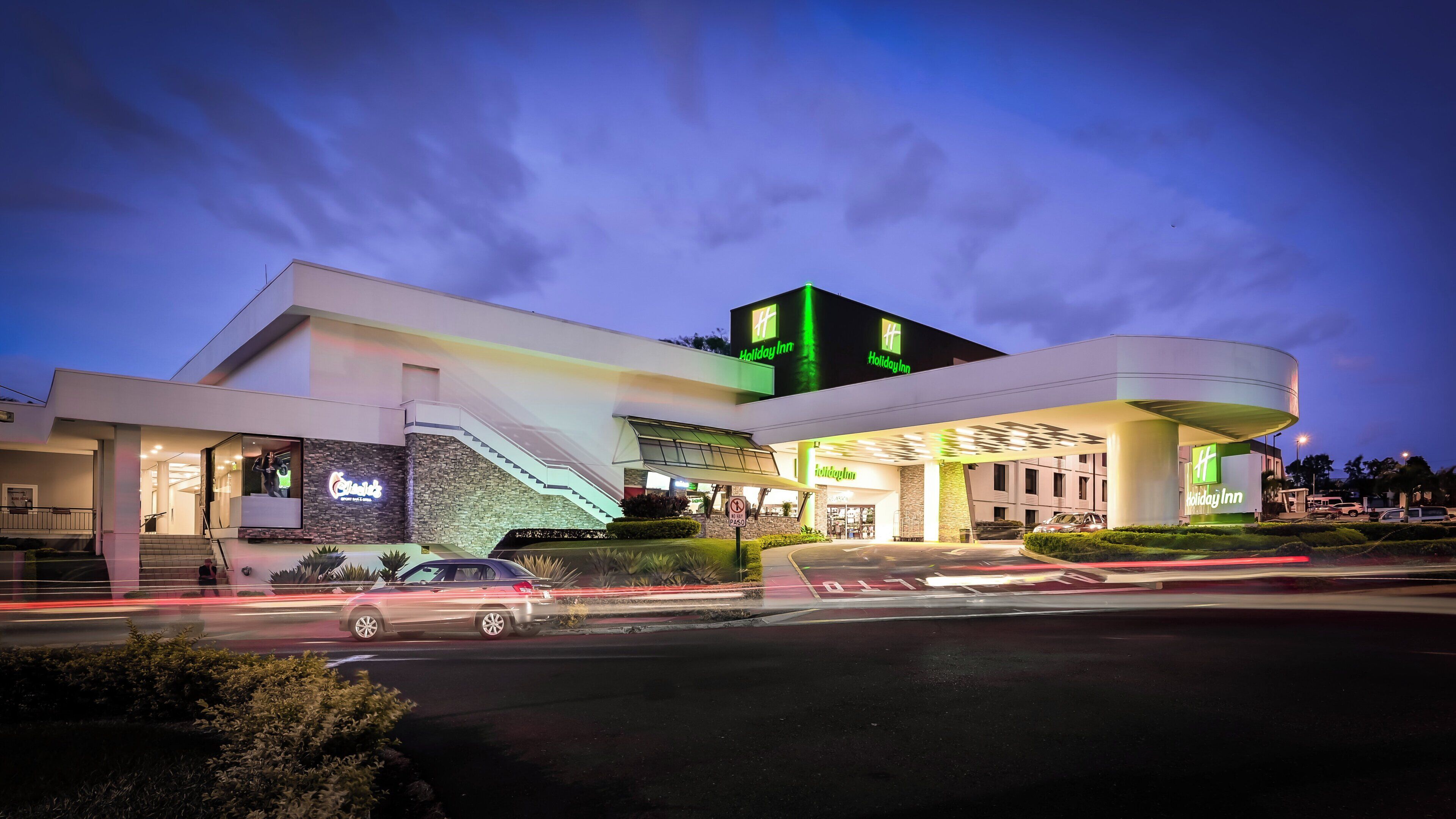 A Holiday Inn hotel with a modern design, featuring a prominent staircase and a large parking area.