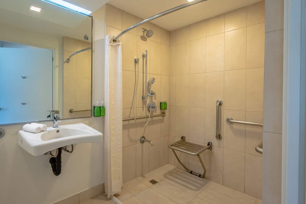 Ein modernes Badezimmer mit Waschbecken, Spiegel, Dusche und Haltegriffen.