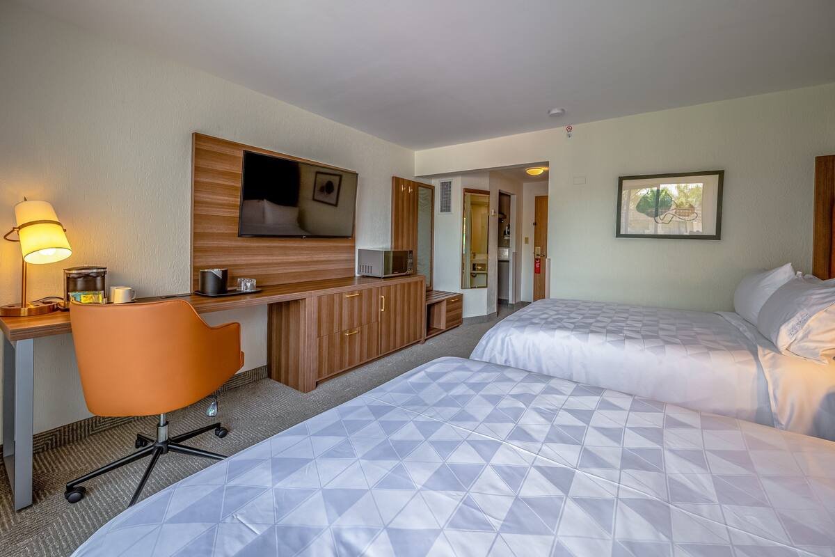 Ein Hotelzimmer mit zwei Betten, einem Schreibtisch mit Stuhl, einer Mikrowelle und einem Fernseher.
