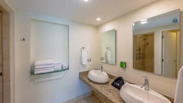 A bathroom with two sinks, a glass shelf with folded towels, a mirror, and a shower area.