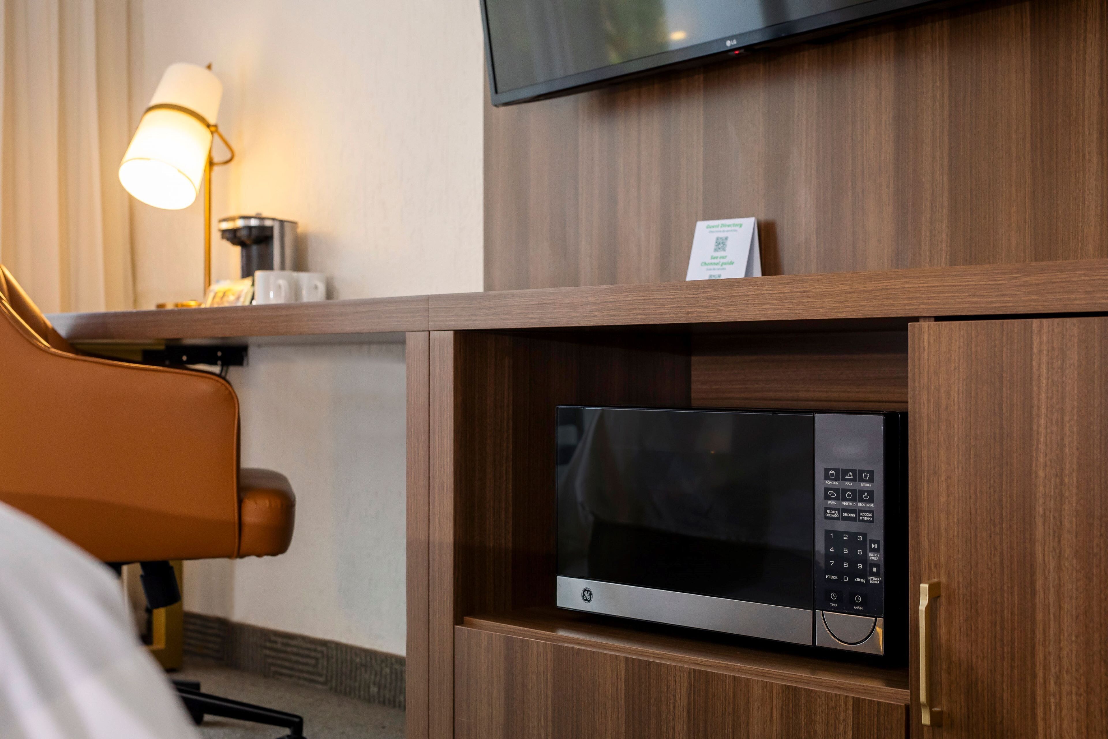 A hotel room with a wooden cabinet containing a microwave, a coffee machine, and a television mounted on the wall.