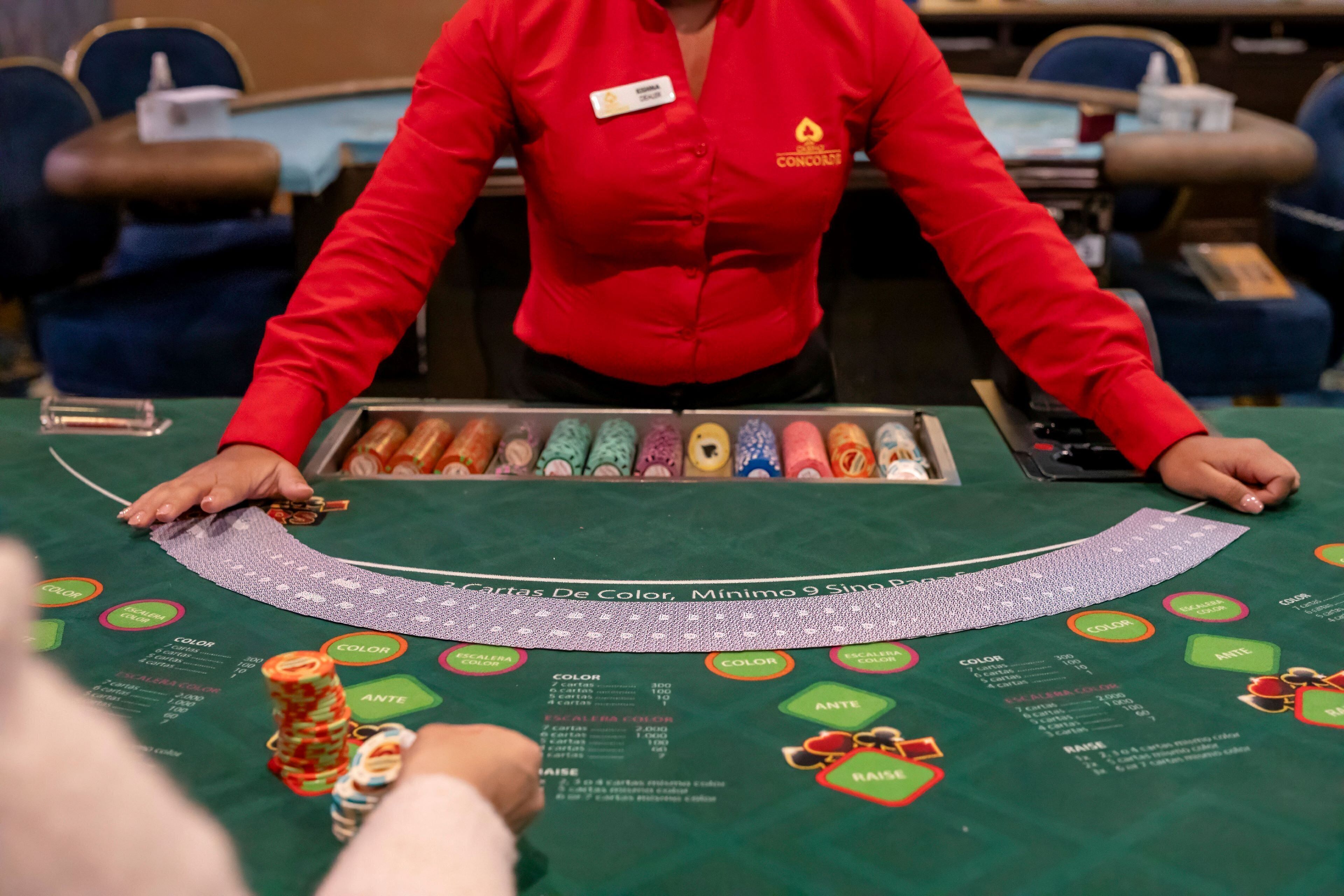 A blackjack table with a dealer in a red shirt, chips, and cards.