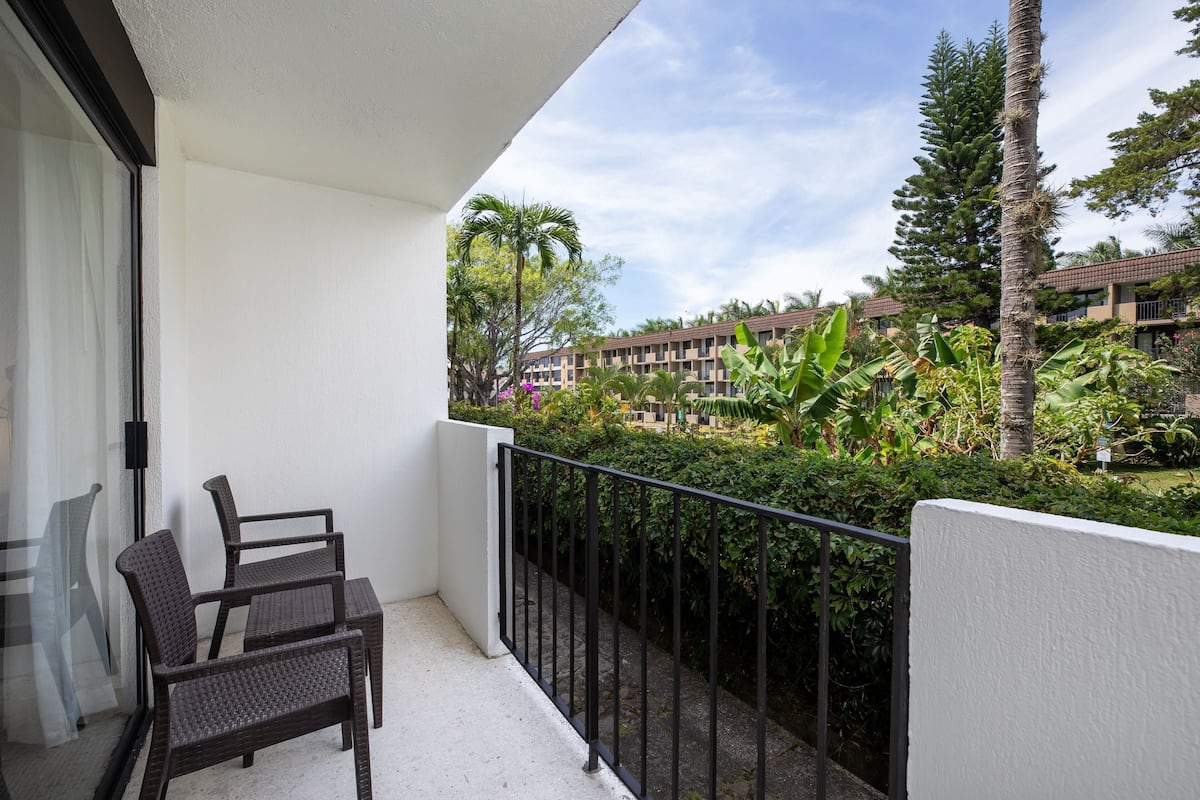 Ein Balkon mit Korbmöbeln, Blick auf einen angelegten Garten und ein Gebäude im Hintergrund.