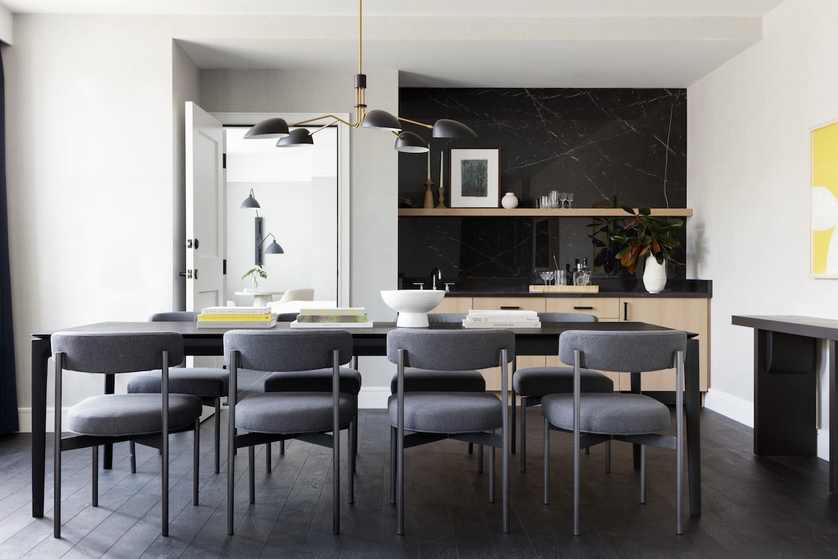 A modern kitchen with a marble backsplash, a dining area with grey chairs, and a black marble countertop.