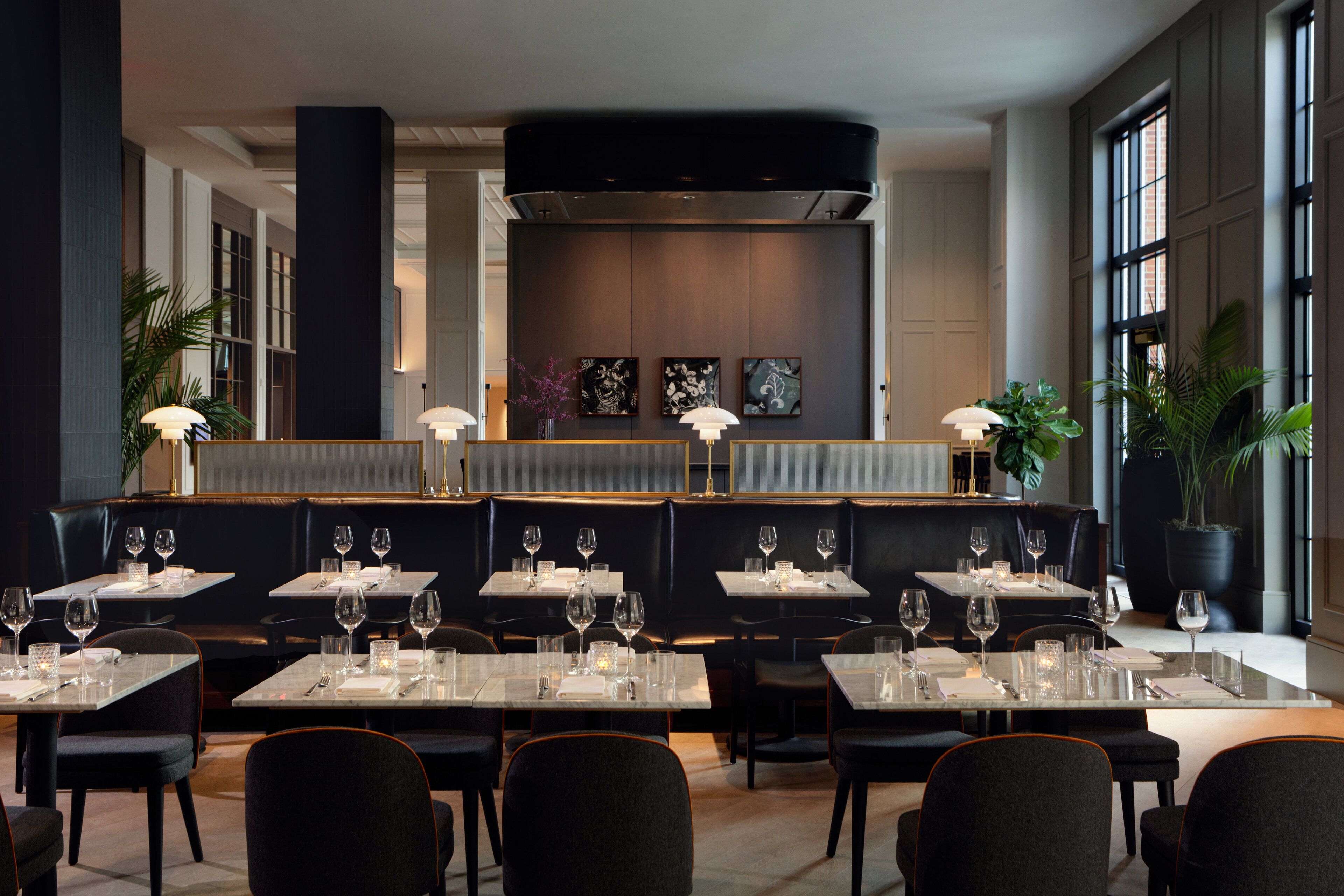 A modern restaurant with tables set for dining, featuring a central bar area and large windows.