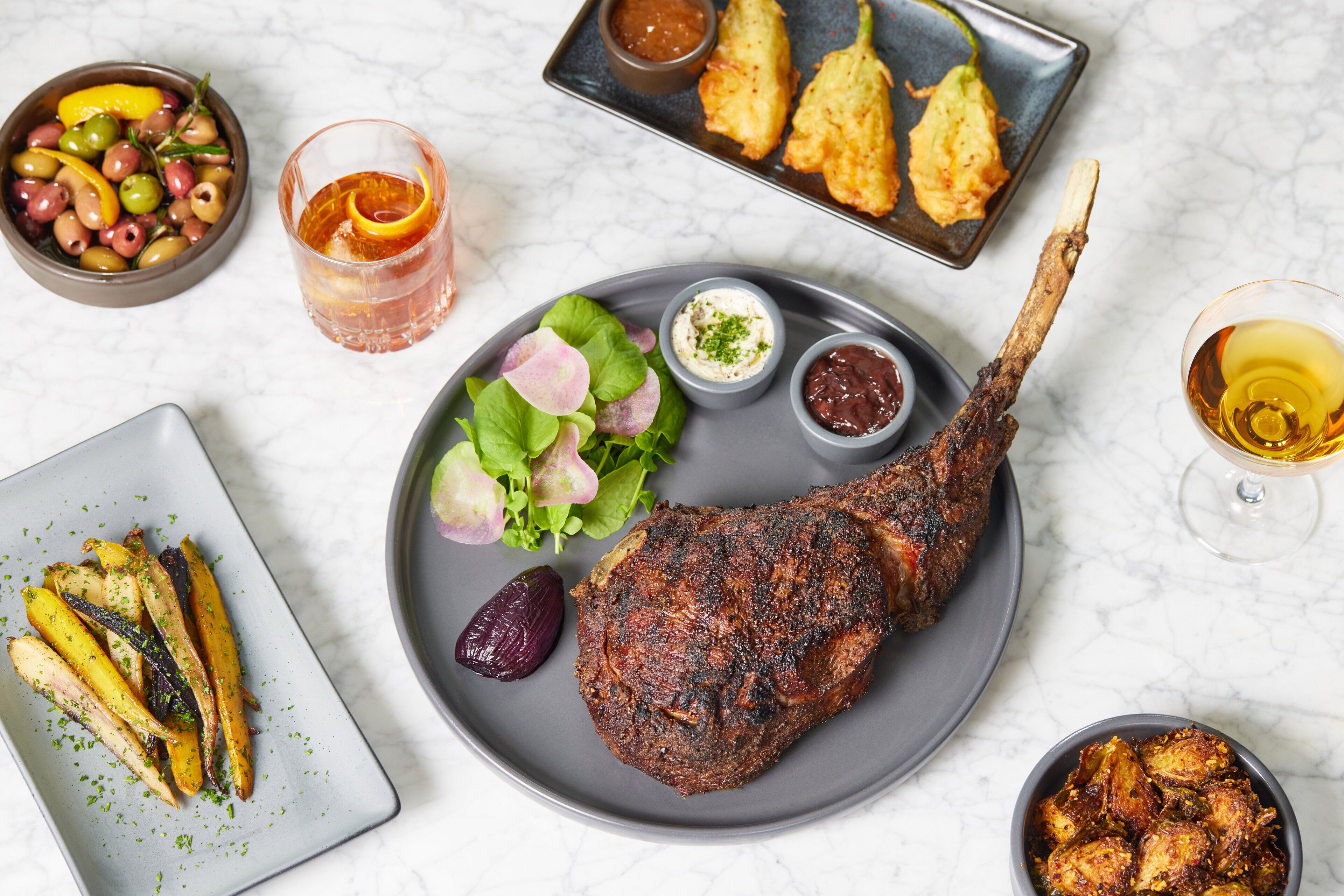 Una mesa de comedor con un cordero asado, diferentes acompañamientos y bebidas.