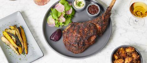 Una mesa de comedor con un cordero asado, diferentes acompañamientos y bebidas.