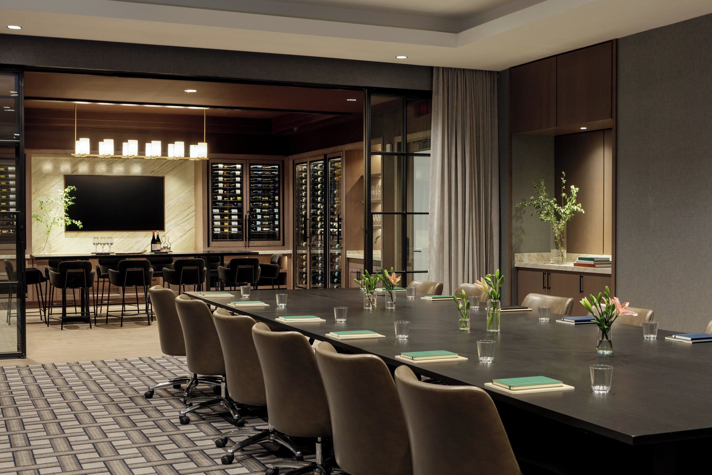 A conference room with a long table, chairs, a television, wine storage, and a plant.