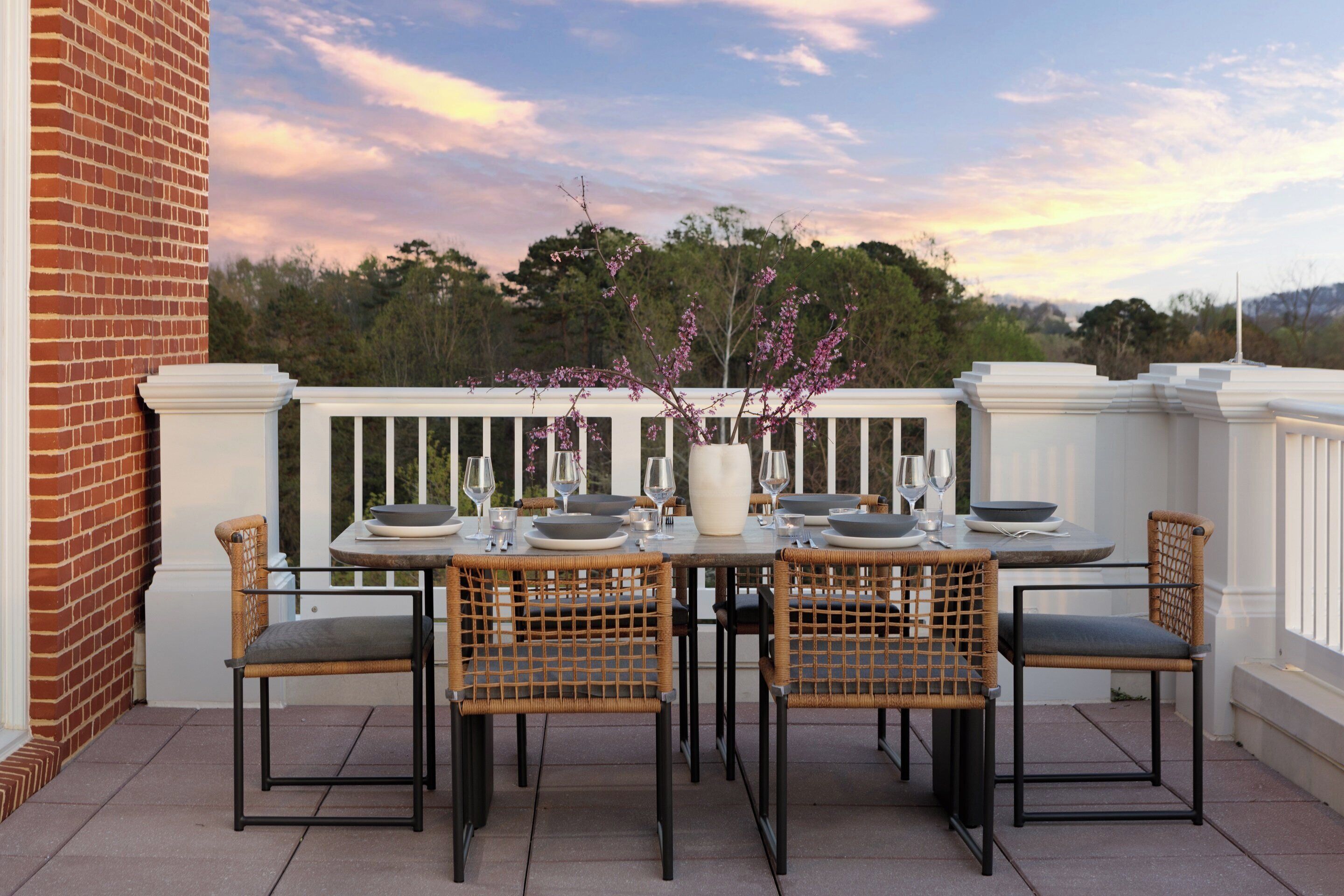 An outdoor dining area with a brick wall, white railing, and wicker chairs.