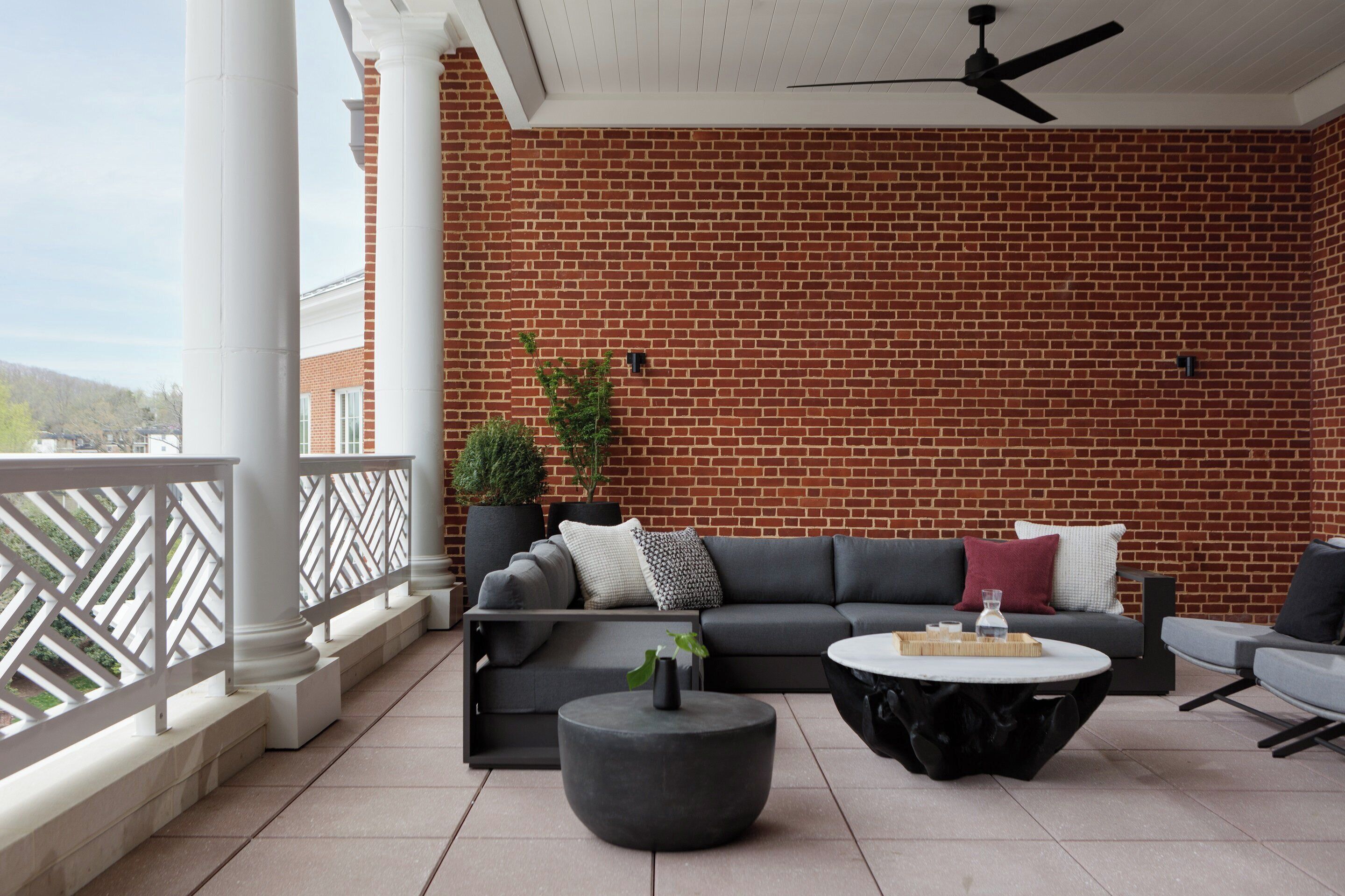 A covered outdoor seating area with a brick wall backdrop, a ceiling fan, and a modern sofa set.