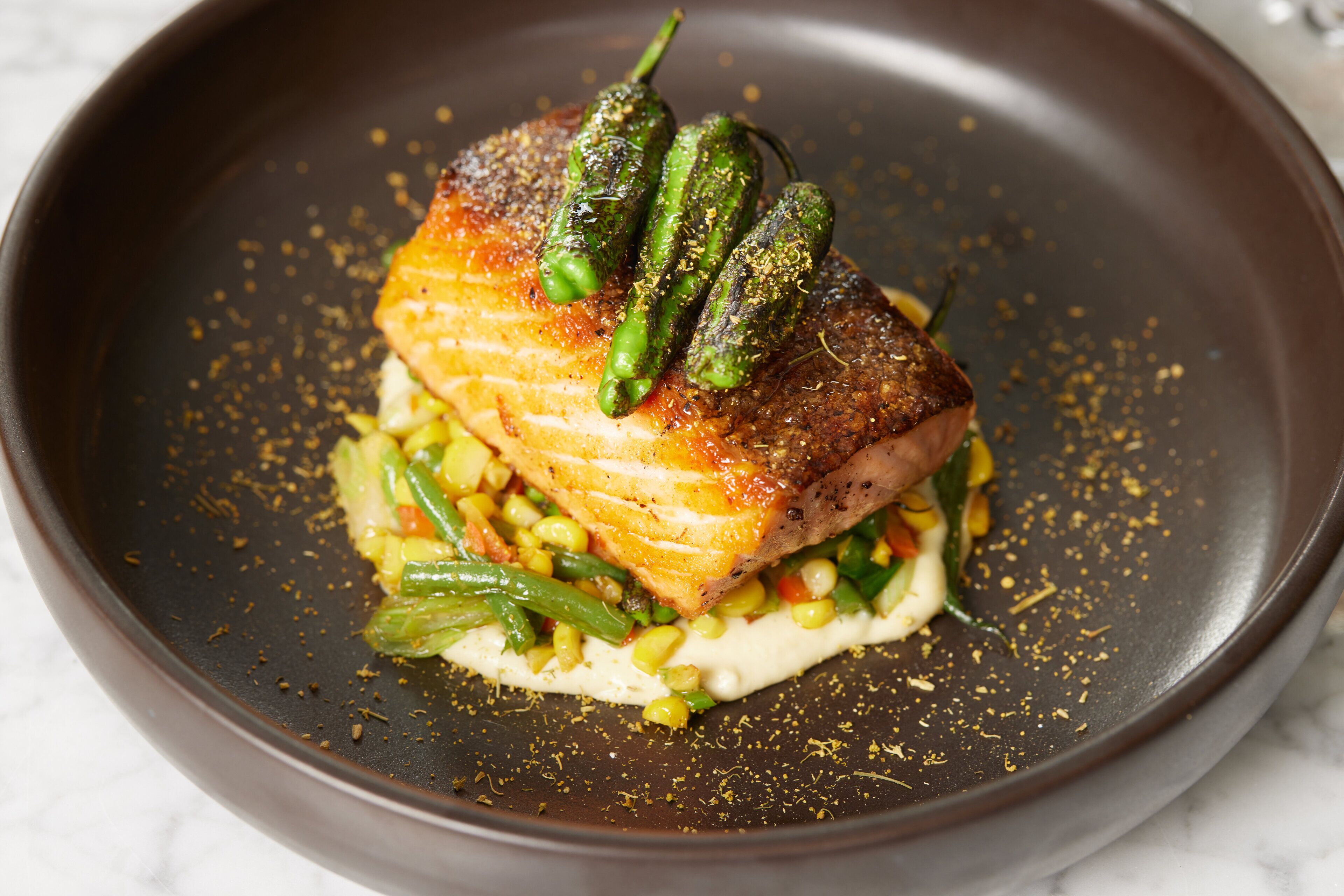 A plate with a piece of meat, green vegetables, and a creamy sauce.