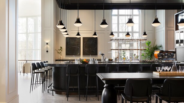 A modern bar area with a long counter, multiple bar stools, and hanging pendant lights. - Kimpton The Forum Hotel by IHG (Charlottesville)