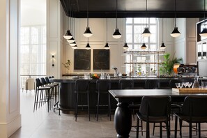 A modern bar area with a long counter, multiple bar stools, and hanging pendant lights. - Kimpton The Forum Hotel by IHG (Charlottesville)