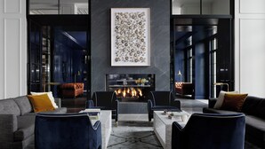 A modern living room with a fireplace, dark blue and grey furniture, and a large abstract painting on the wall. - Kimpton The Forum Hotel by IHG (Charlottesville)