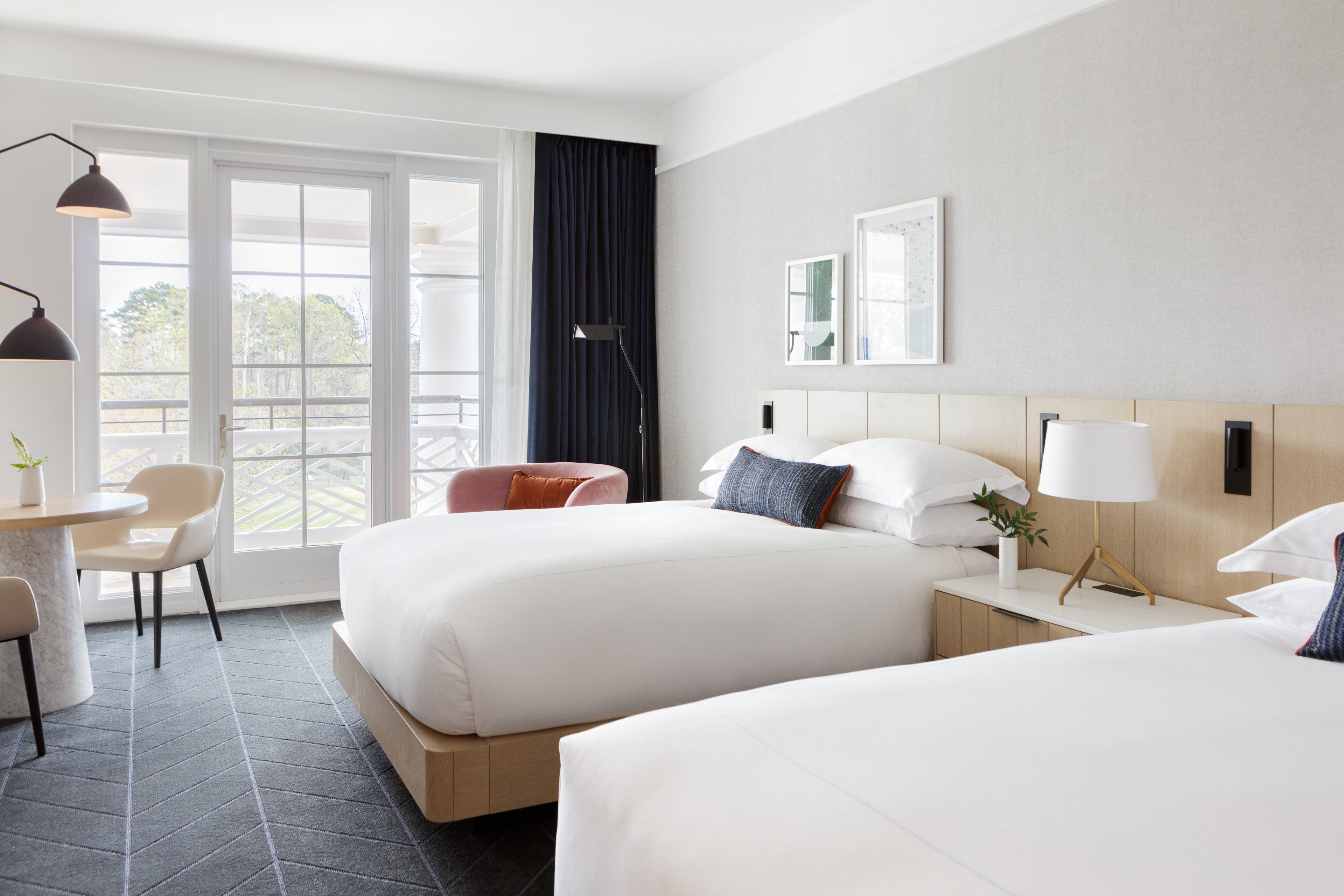 Une chambre d’hôtel avec deux lits, un bureau, une chaise et une grande fenêtre avec des rideaux.