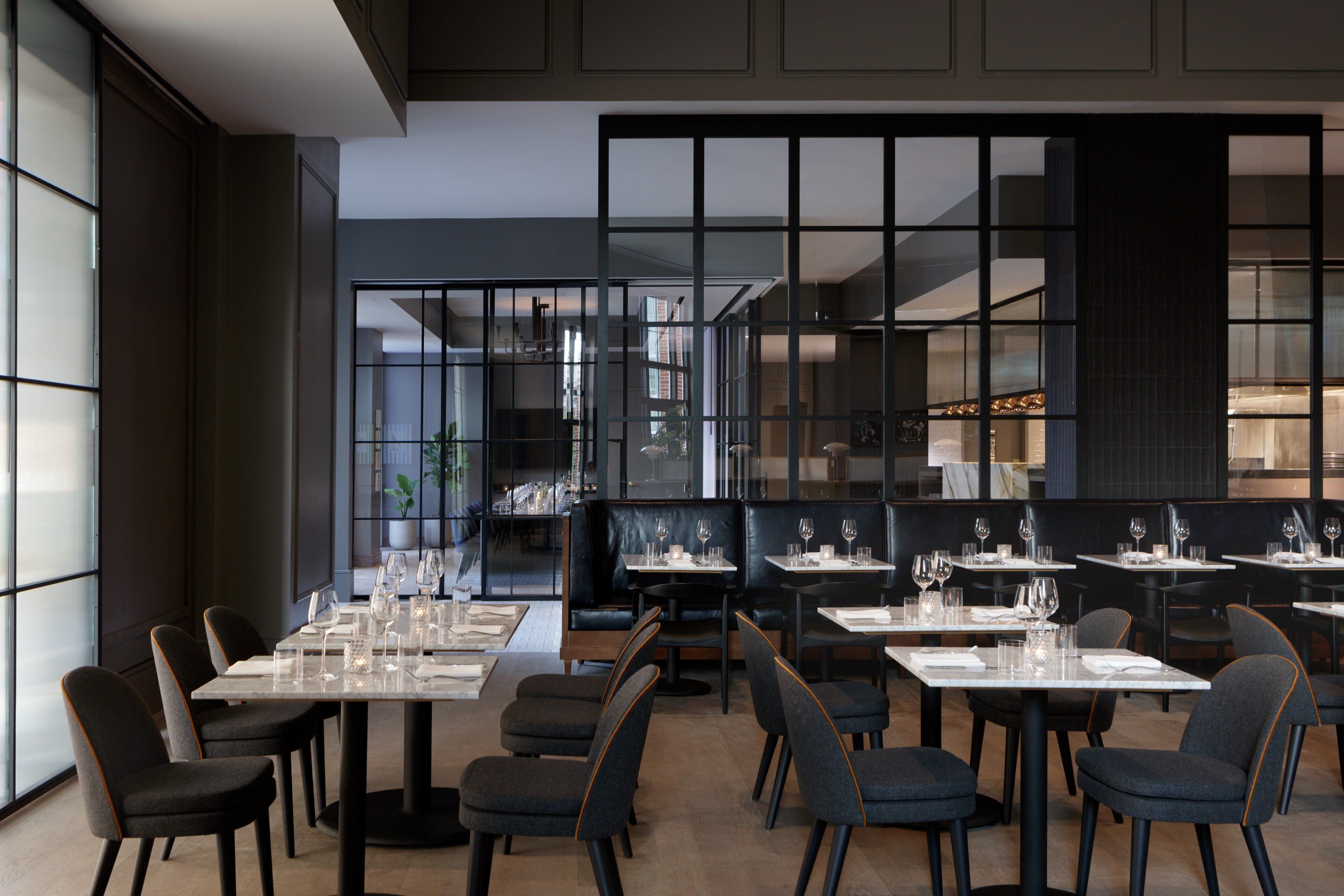 A modern restaurant interior with multiple dining tables and chairs, a large window, and a view of the cityscape.