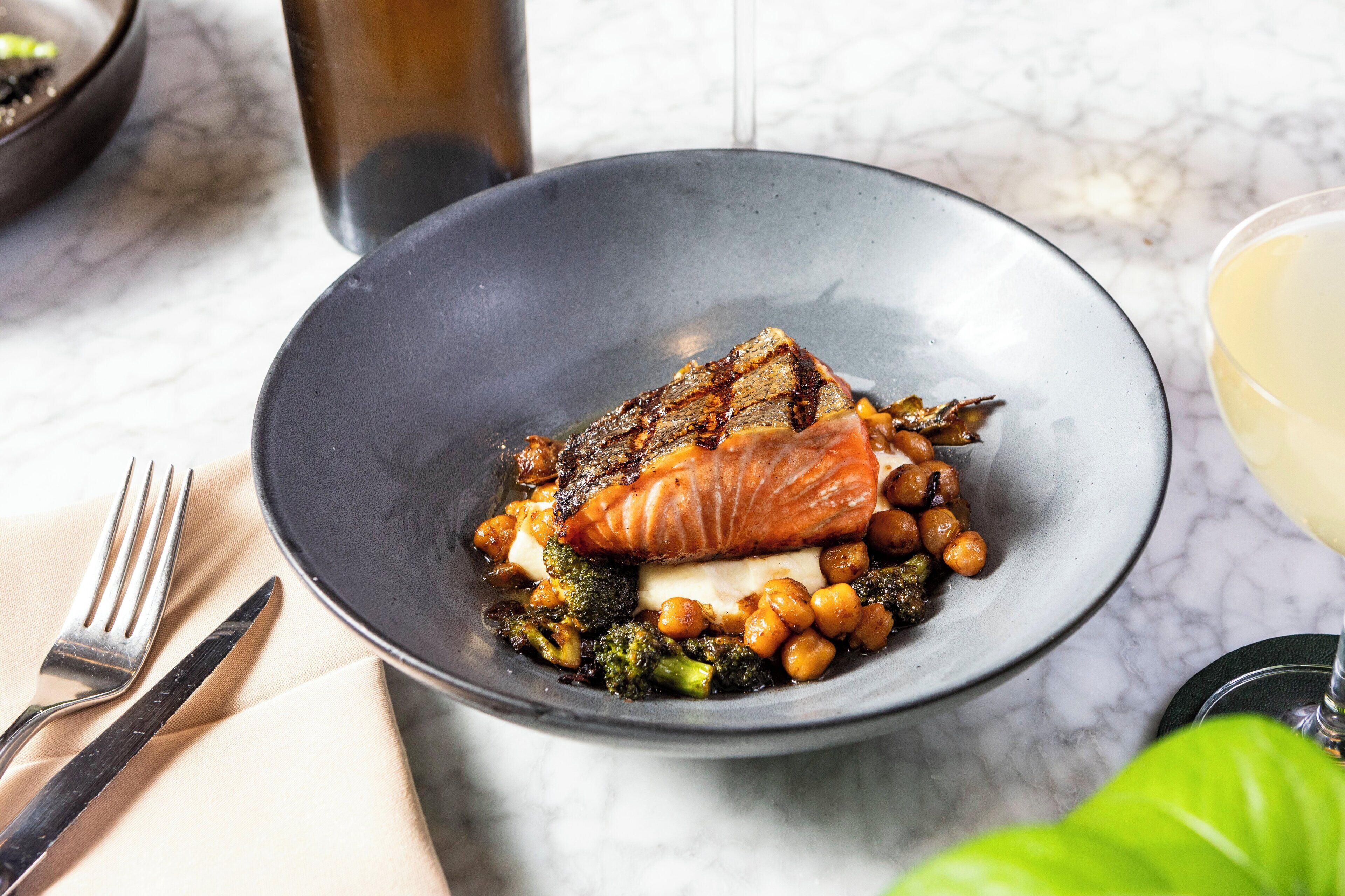 A plate with salmon, chickpeas, and broccoli on a marble table.