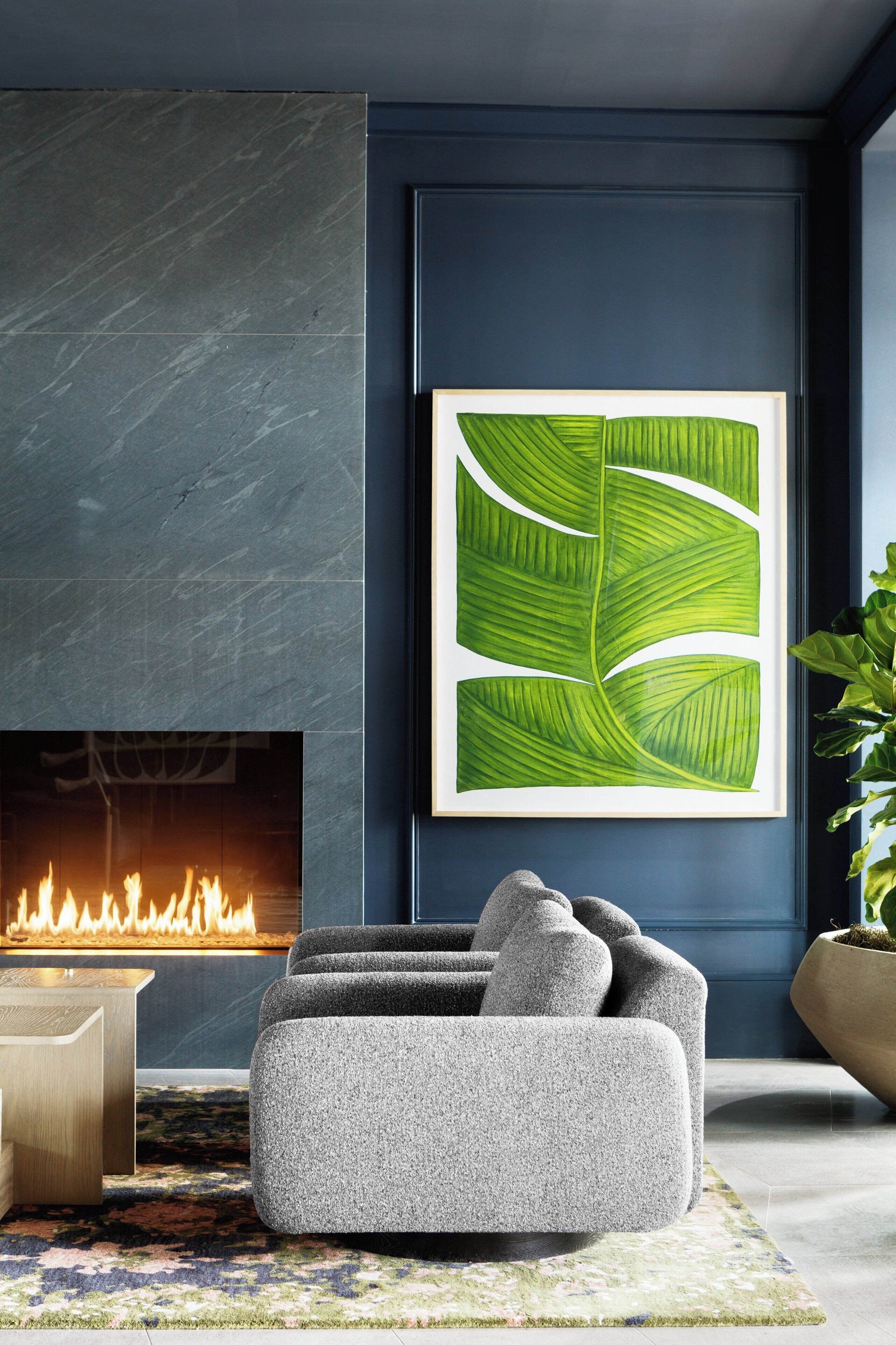 A modern living room with a fireplace, a large green leaf artwork, and a grey sofa.