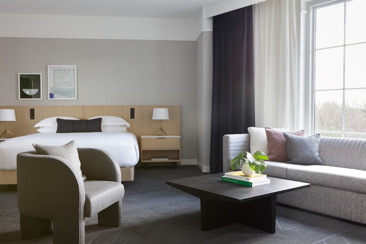 A hotel room with a bed, a sofa, a chair, a coffee table, and a window with curtains.