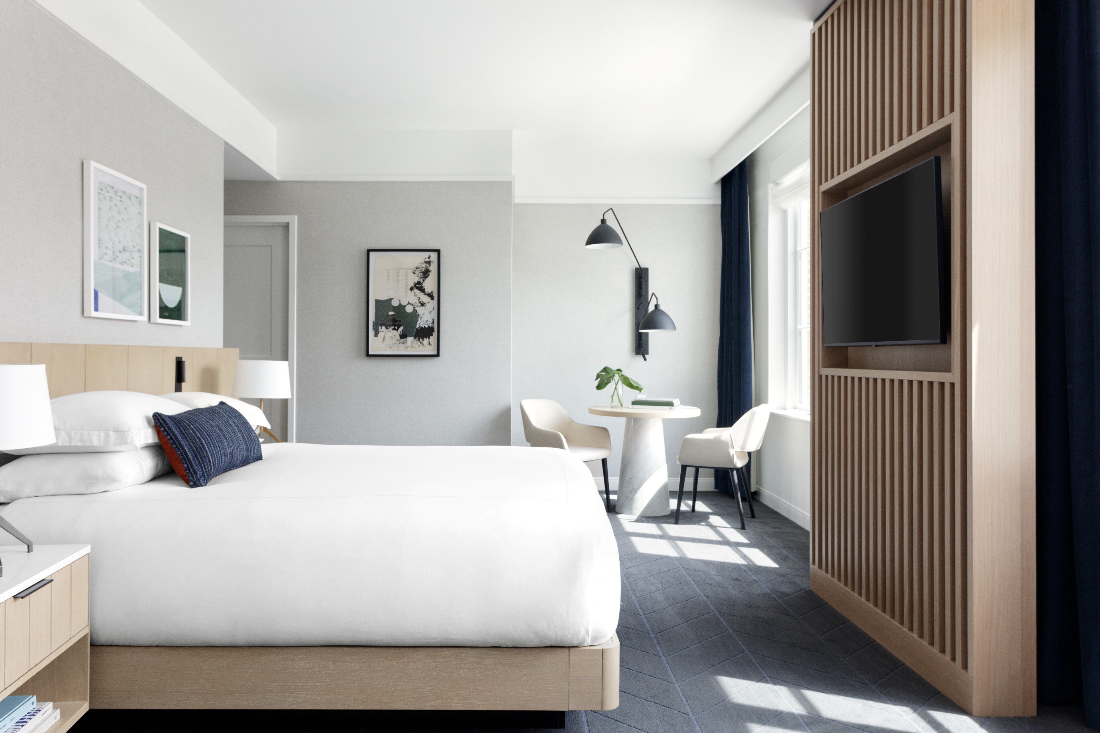 Una habitación de hotel moderna con una cama grande, mesitas de noche, un escritorio, una silla, un televisor y obras de arte en las paredes.