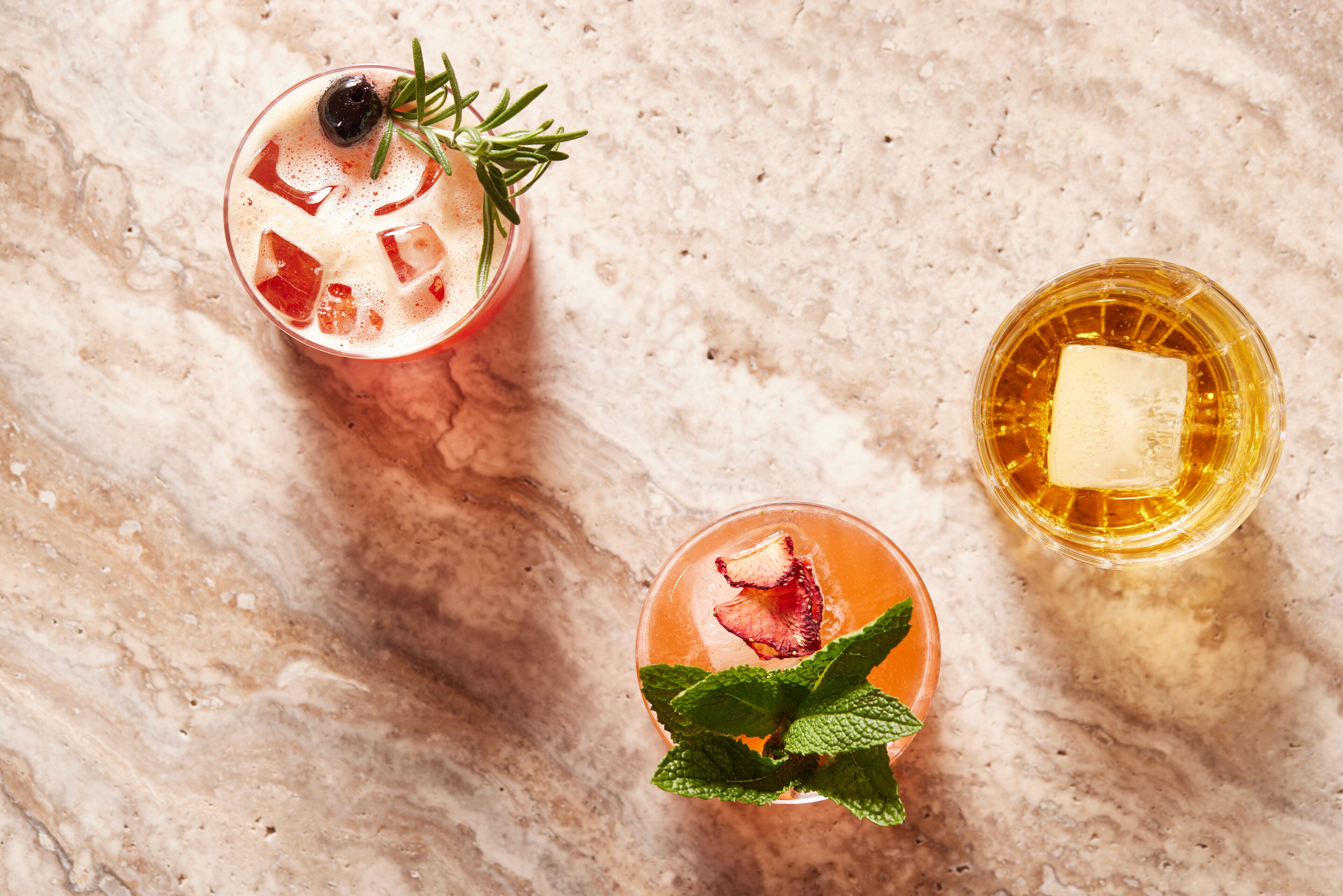 Three glasses of beverages on a marble surface.