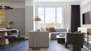 Una sala de estar moderna con un sofá, sillones, una mesa de centro y un televisor. Hay un comedor con sillas y una mesa, y un ventanal que ofrece vistas al exterior.