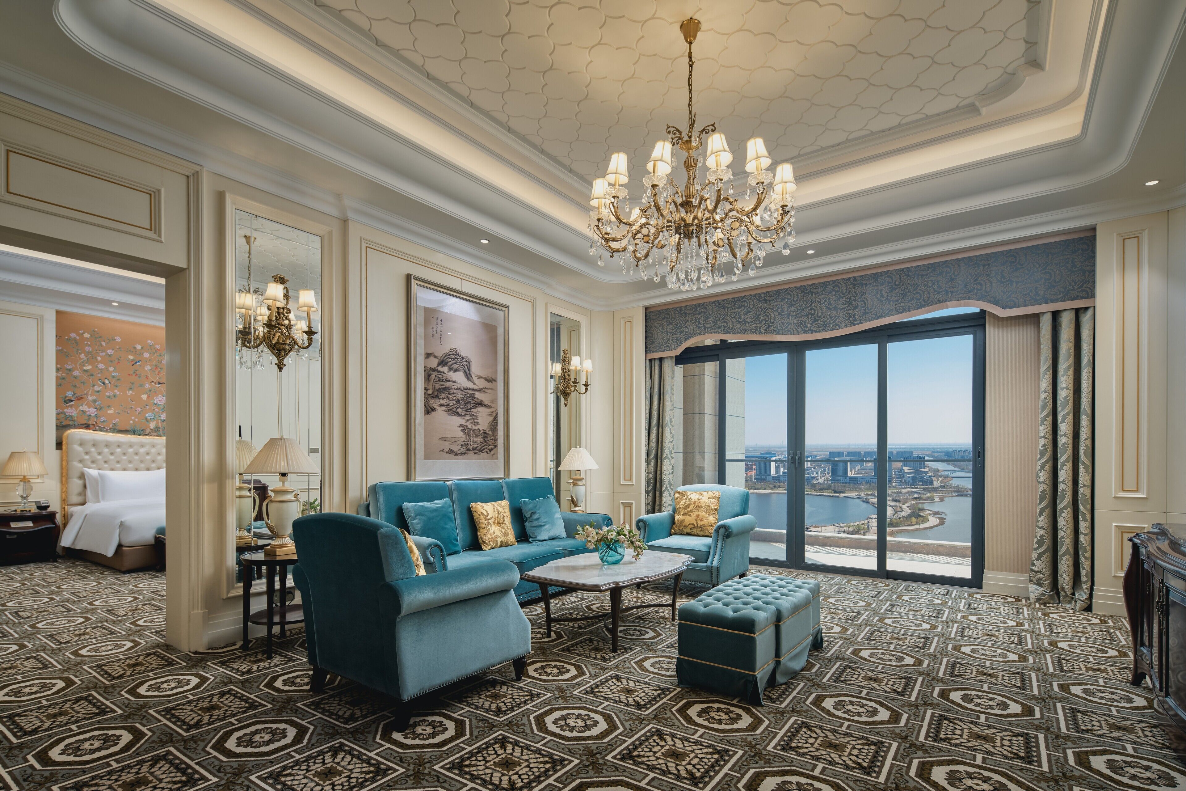 Une chambre d’hôtel luxueuse, dotée d’un grand lit, d’un canapé bleu, d’une table basse et offrant une vue sur le paysage urbain grâce à de grandes fenêtres.