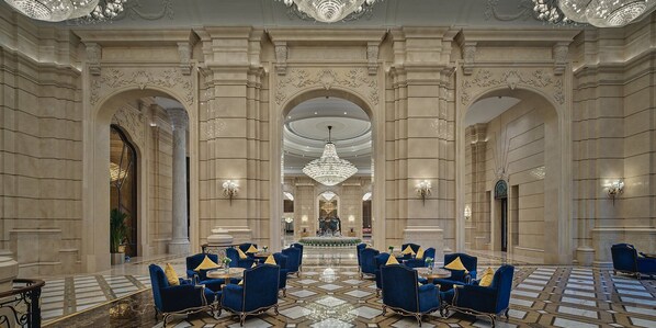 A grand lobby with high ceilings, ornate columns, and a central chandelier.