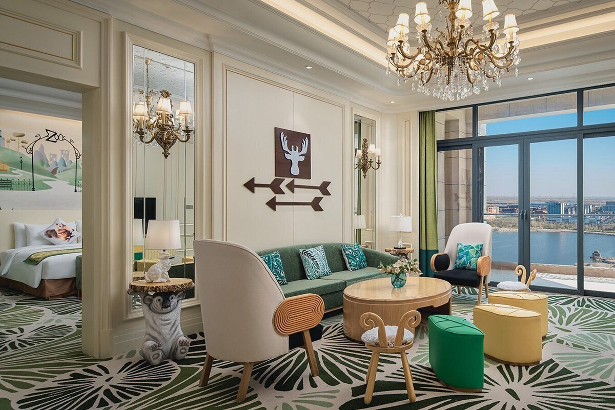 Une chambre d’hôtel spacieuse dotée d’une grande fenêtre donnant sur la ville, d’un canapé vert, d’une table basse ronde et d’un téléviseur.