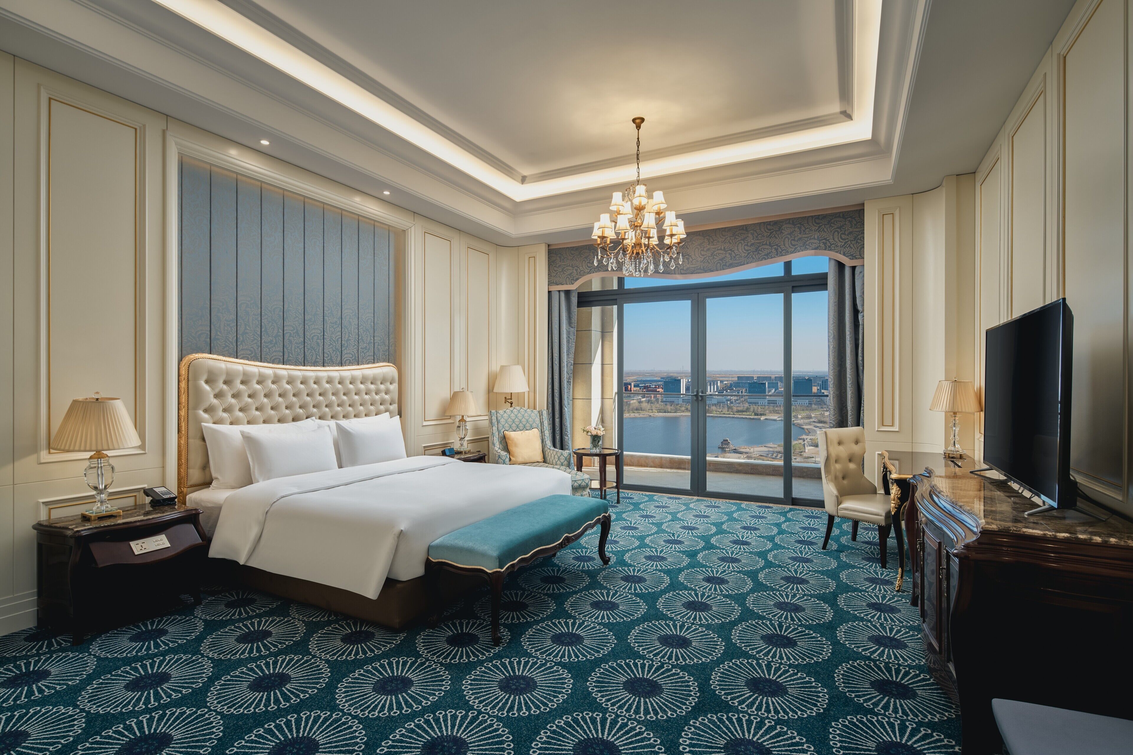 A hotel room with a large bed, a television, a desk, and a view of the city.