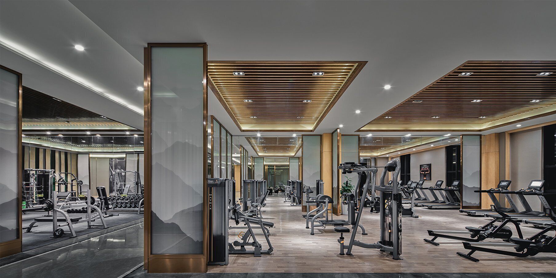 Un gimnasio moderno con diverso equipamiento de ejercicio, una columna central y un muro con espejos.