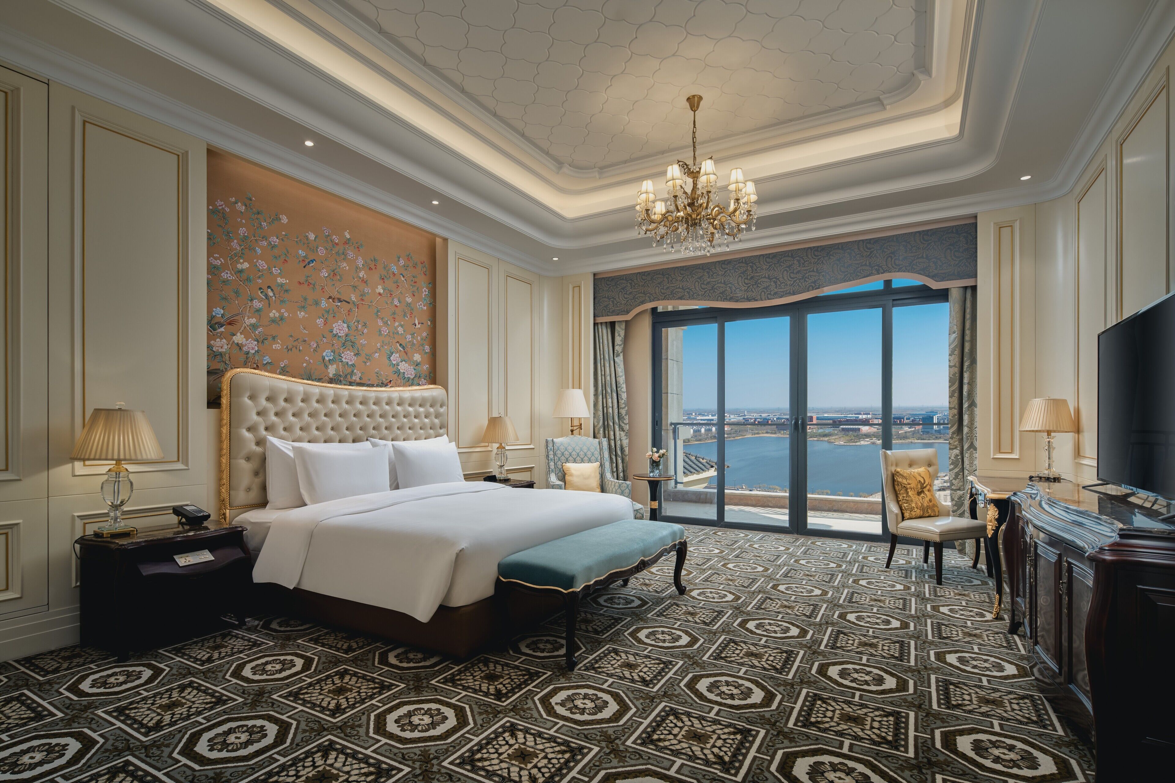 Een luxe hotelkamer met een groot bed, een kroonluchter, stadszicht en een balkon.