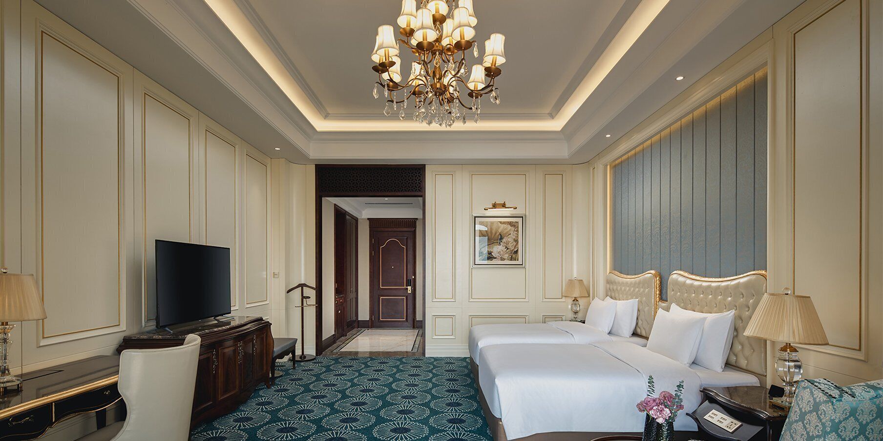A hotel room with a large bed, a television, a desk, and a chandelier.