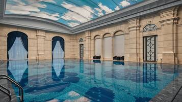 Una piscina interior con superficie de agua azul cristalina, rodeada de arquitectura clásica con columnas y arcos.