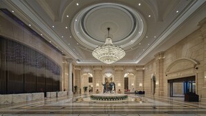 Een ruime lobby met een statige kroonluchter, marmeren vloeren en klassieke architectuur.