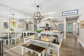 Una cocina moderna con armarios blancos, una isla central y un comedor con sillas blancas y una mesa de madera.