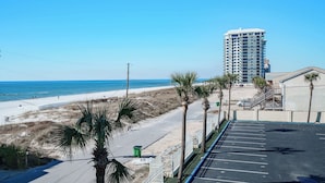 A parking lot adjacent to a beach with a high-rise building in the background. - Bethys Beachy Beauty Regency Towers! (Panama City Beach)