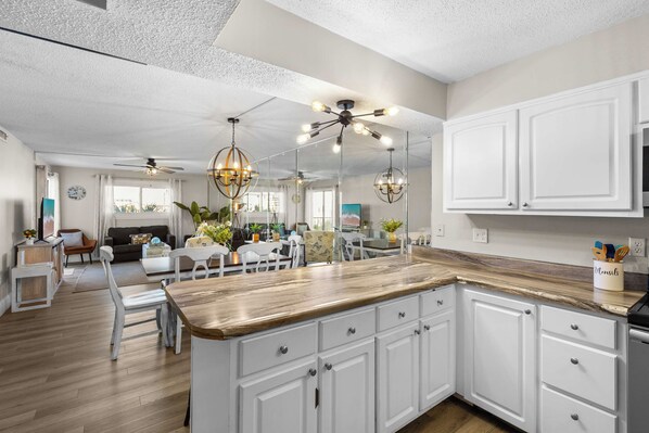 A modern kitchen with white cabinetry, a wooden countertop, and pendant lighting.