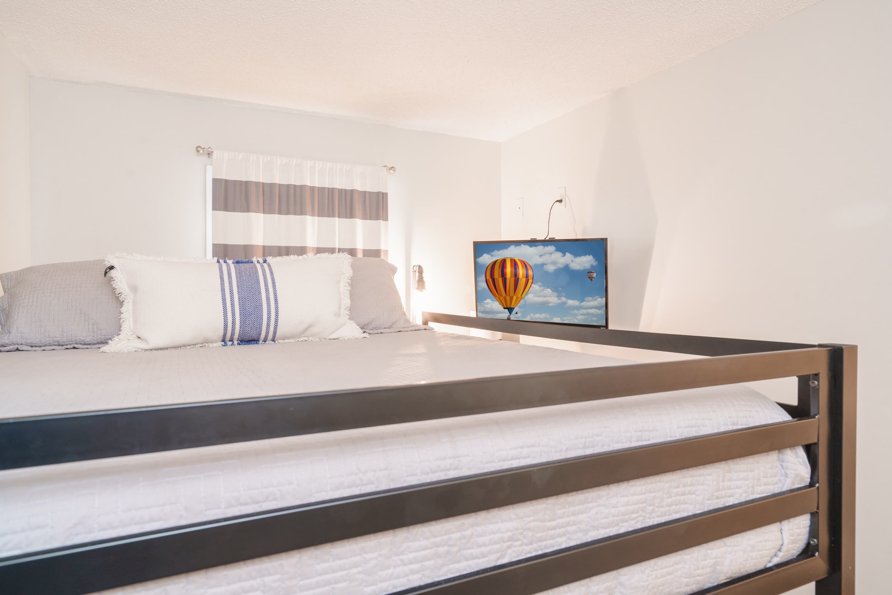Une chambre avec un lit superposé, une fenêtre avec des rideaux à rayures et un tableau encadré représentant une montgolfière.
