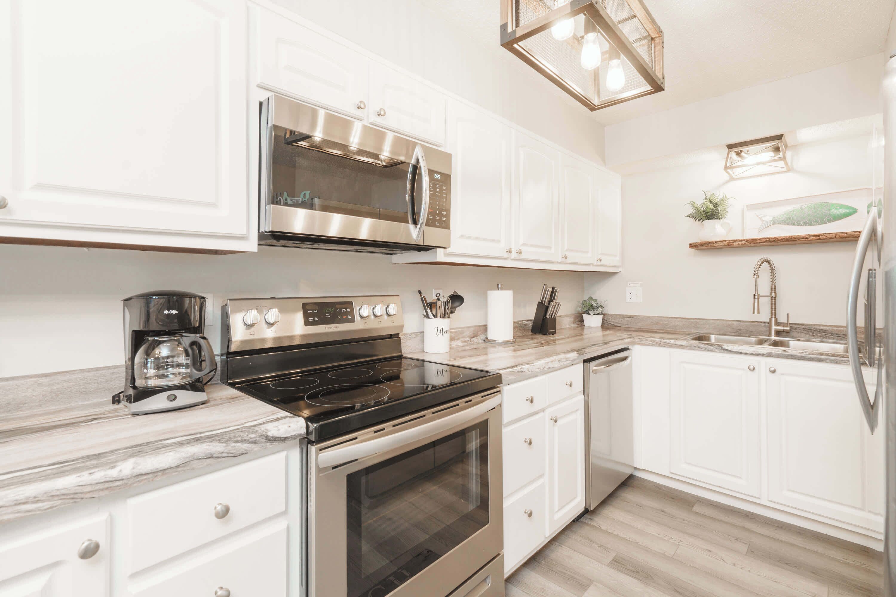 A modern kitchen with white cabinets, stainless steel appliances, and a marble countertop.