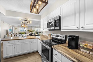 A modern kitchen with white cabinetry, a central island, a built-in oven, a microwave, and a coffee maker.