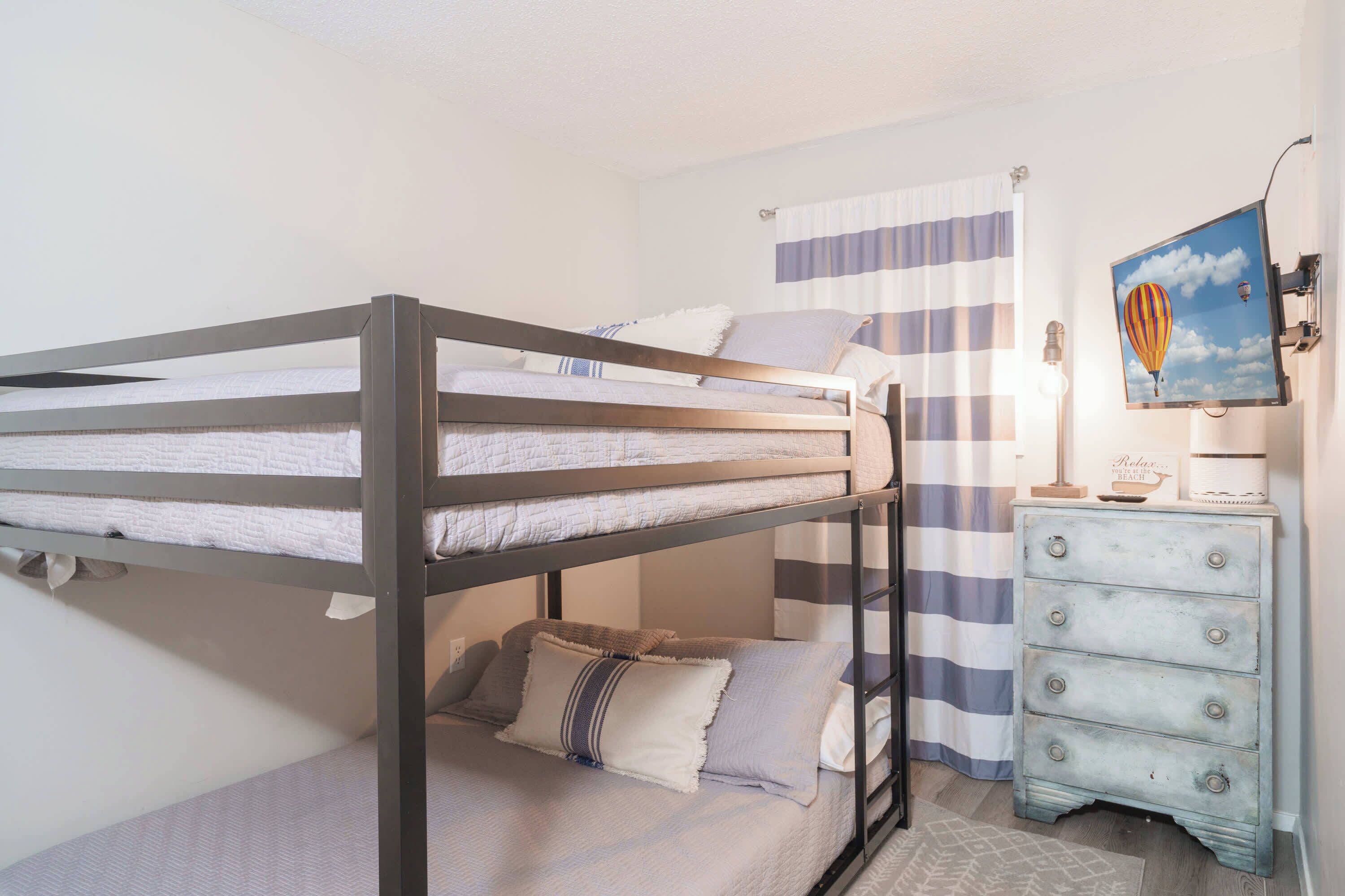 A bunk bed with a lower bunk, a dresser with drawers, a striped curtain, and a framed picture of a hot air balloon.