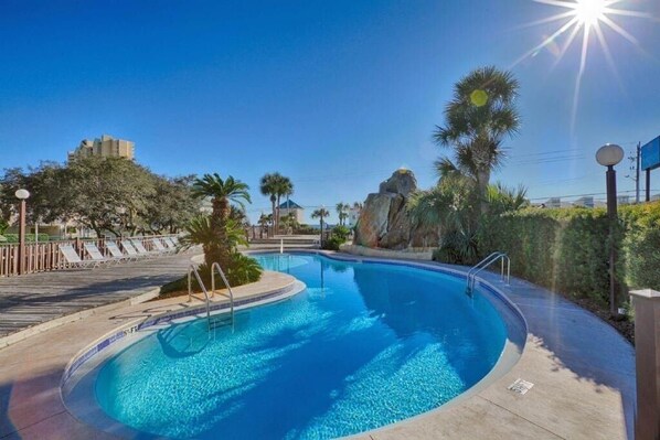 A swimming pool with a curved edge, surrounded by palm trees and a rock formation.