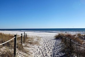 A sandy beach path leading to the ocean with wooden posts and ropes marking the boundary.